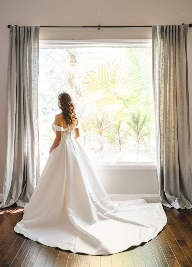 Bride wearing elegant wedding dress while staring out the window