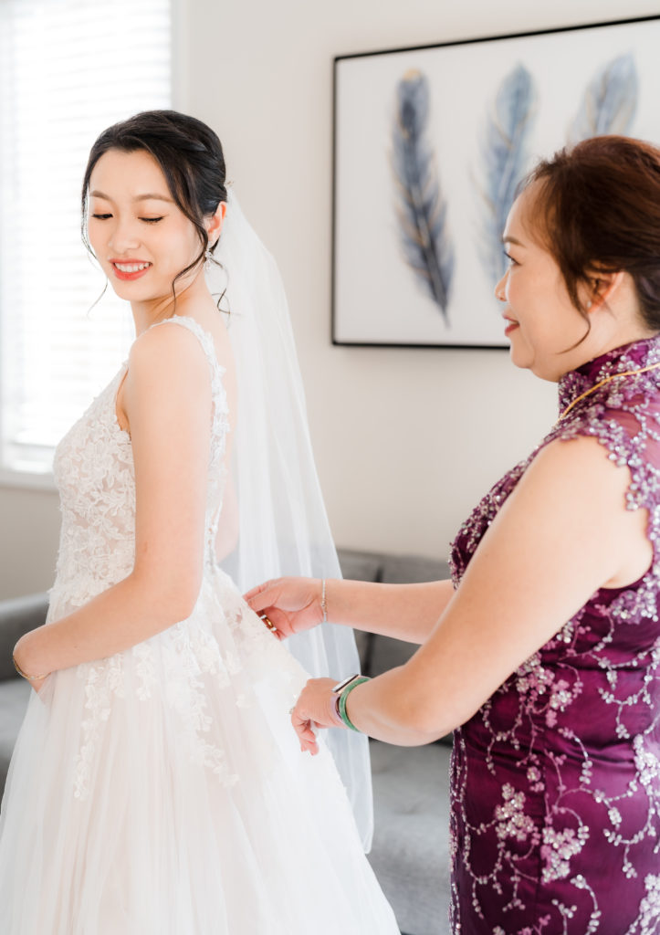 Mom helping Bride zip up dress before Elegant Wedding in California
