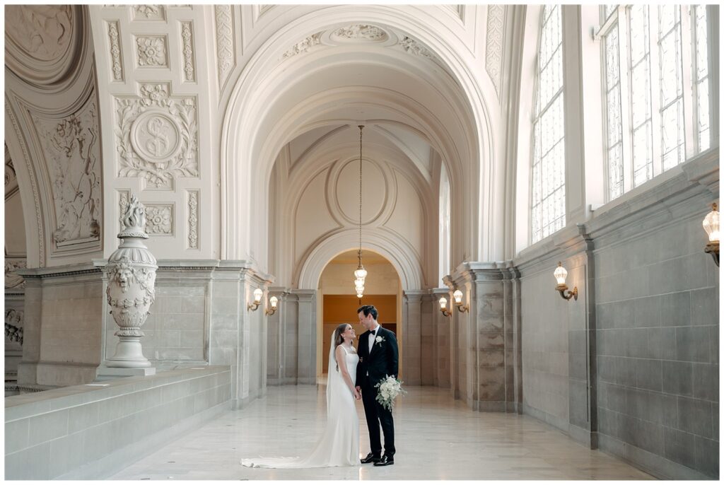 San Francisco City Hall wedding portrait of a couple standing beneath elegant archways and soft light, captured by Helena Wong Photography